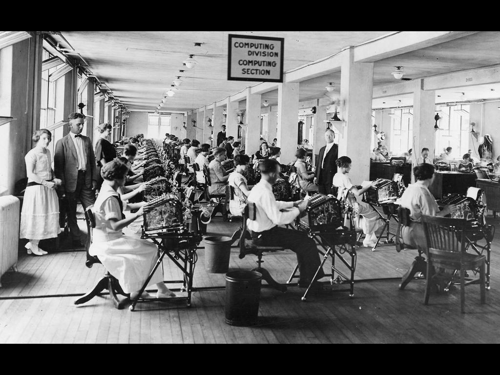 People in an old office sitting at mechanical calculator machines