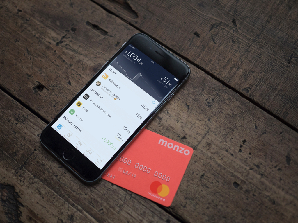 Monzo promotional image showing app on an iPhone and their distinctive coral coloured debit card
